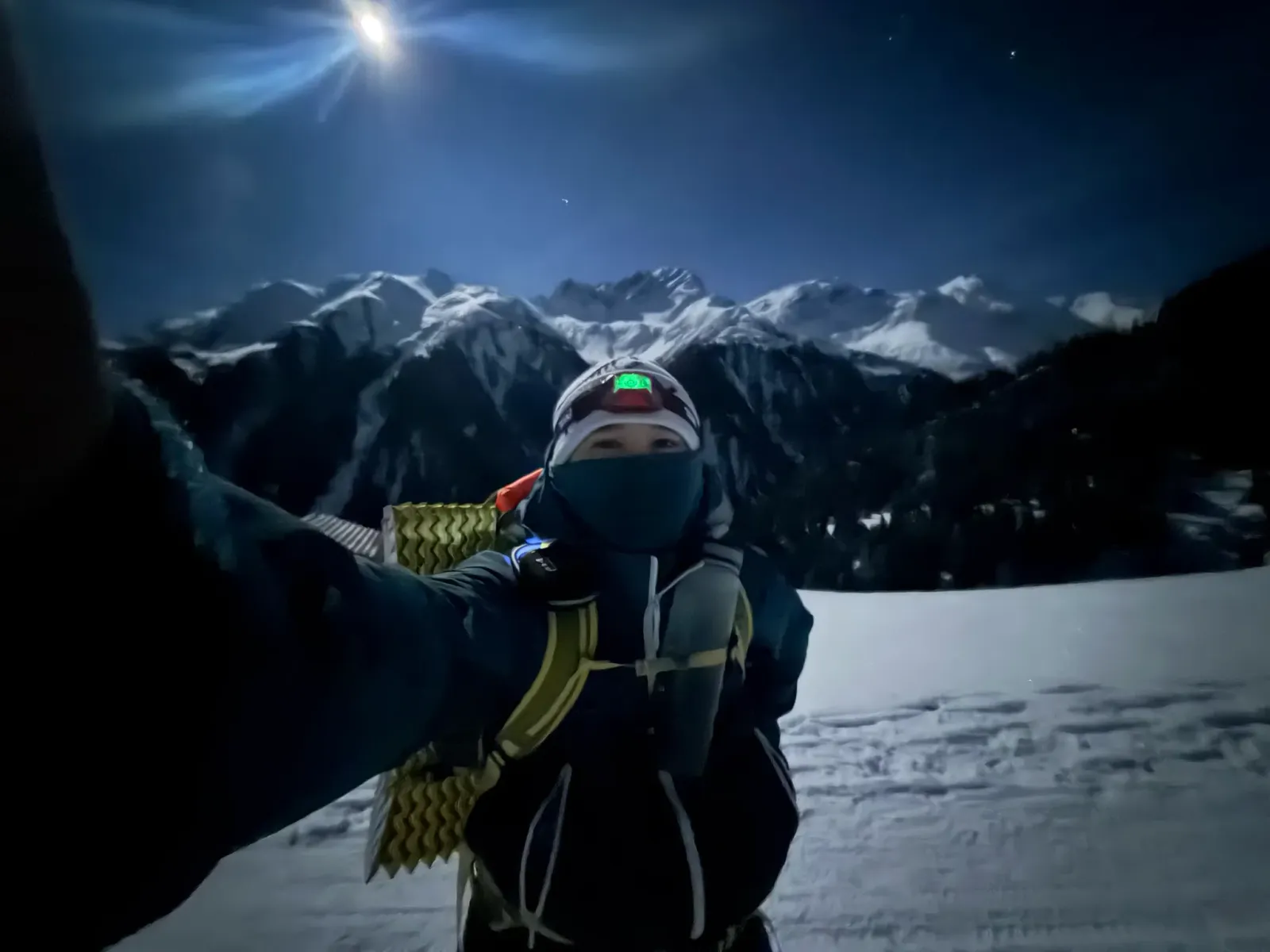 a night selfie on a snow slope, the moon and a mountain range behind